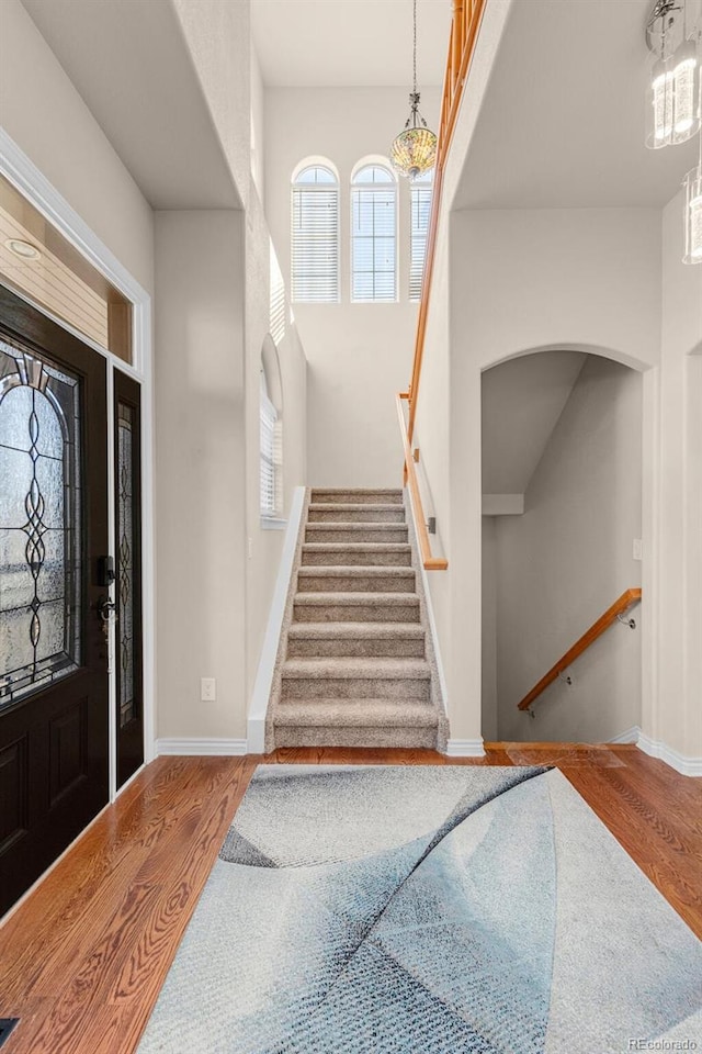 entrance foyer featuring arched walkways, stairway, wood finished floors, and baseboards