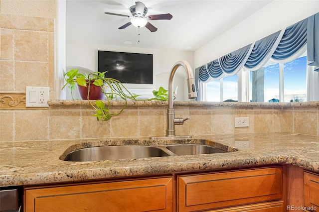 kitchen with light stone counters, brown cabinetry, a sink, and a ceiling fan