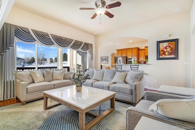 living area with arched walkways, ceiling fan, and wood finished floors