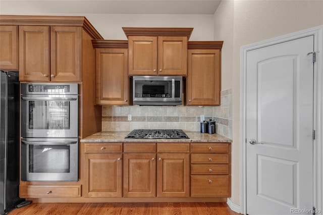 kitchen with appliances with stainless steel finishes, brown cabinets, light wood-style flooring, and decorative backsplash