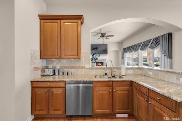 kitchen with ceiling fan, light stone counters, a sink, stainless steel dishwasher, and decorative backsplash