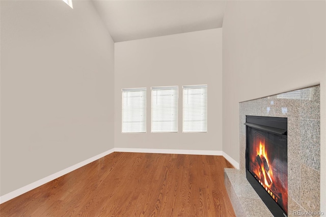 unfurnished living room featuring a tile fireplace, baseboards, and wood finished floors