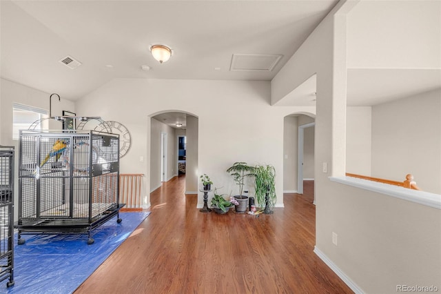 interior space featuring baseboards, visible vents, arched walkways, lofted ceiling, and wood finished floors