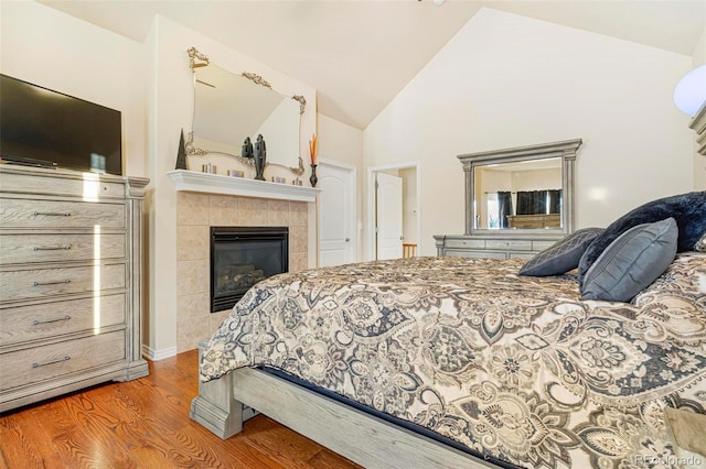 bedroom with a tiled fireplace, high vaulted ceiling, and wood finished floors