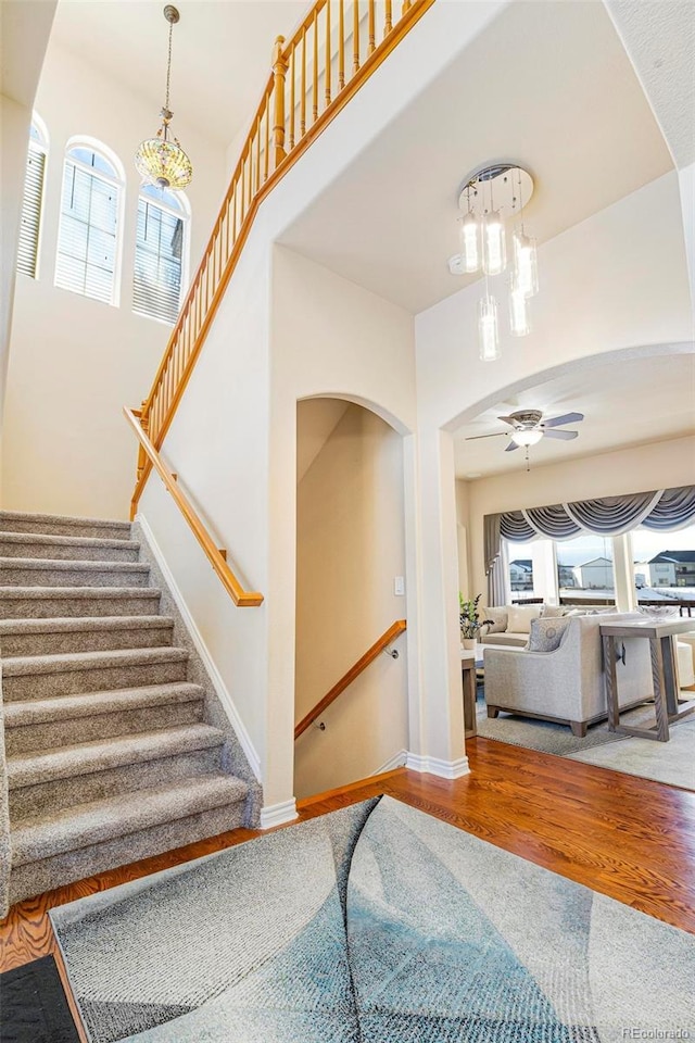 stairs featuring baseboards, wood finished floors, a ceiling fan, and a healthy amount of sunlight