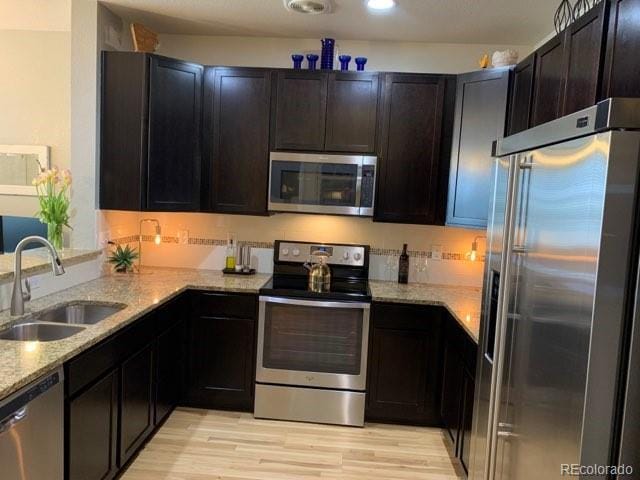 kitchen with light hardwood / wood-style flooring, sink, stainless steel appliances, and light stone counters