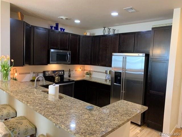 kitchen with appliances with stainless steel finishes, light wood-type flooring, and light stone countertops