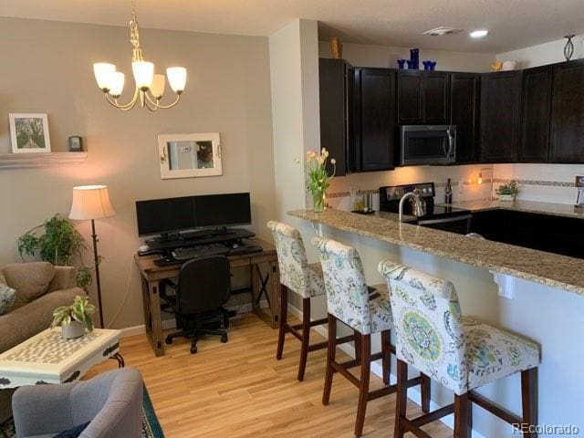 kitchen featuring light stone counters, a chandelier, a kitchen breakfast bar, light hardwood / wood-style floors, and electric range