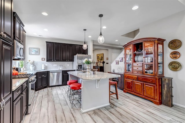 5519 Genoa St, Denver, CO 80249 - kitchen featuring stainless steel appliances, light wood-style floors, a breakfast bar area, a kitchen island, and backsplash