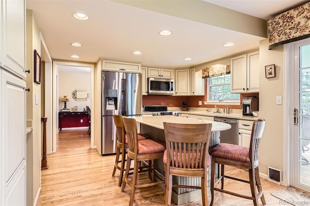 kitchen featuring a breakfast bar area, a kitchen island, light wood-type flooring, light countertops, and stainless steel appliances