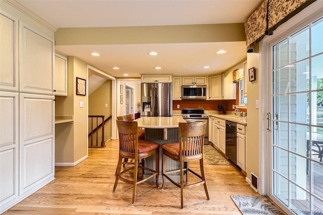 kitchen featuring a breakfast bar area, a center island, light countertops, light wood finished floors, and stainless steel appliances
