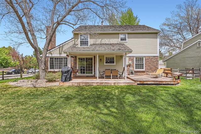 rear view of house with a lawn, fence, a deck, and brick siding