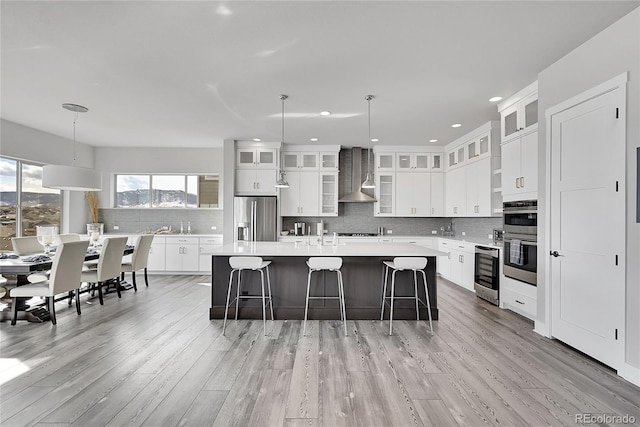 kitchen featuring white cabinets, a center island, wall chimney exhaust hood, appliances with stainless steel finishes, and pendant lighting