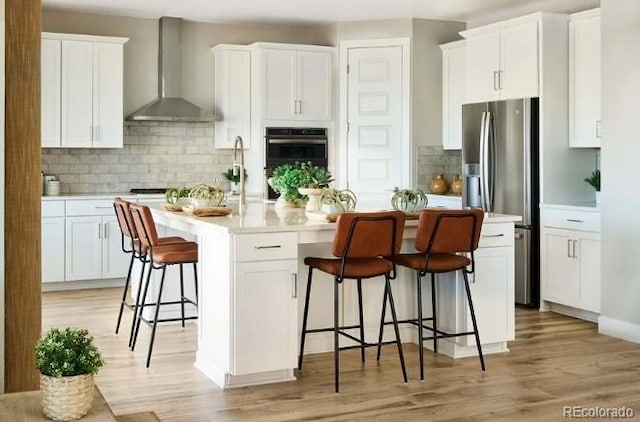 3343 N Catawba Way, Aurora, CO 80019 - kitchen featuring multiple ovens, stainless steel fridge, a kitchen breakfast bar, wall chimney range hood, and an island with sink