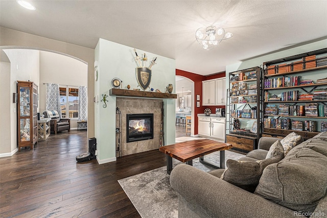 living room with dark wood-type flooring, arched walkways, baseboards, and a tiled fireplace