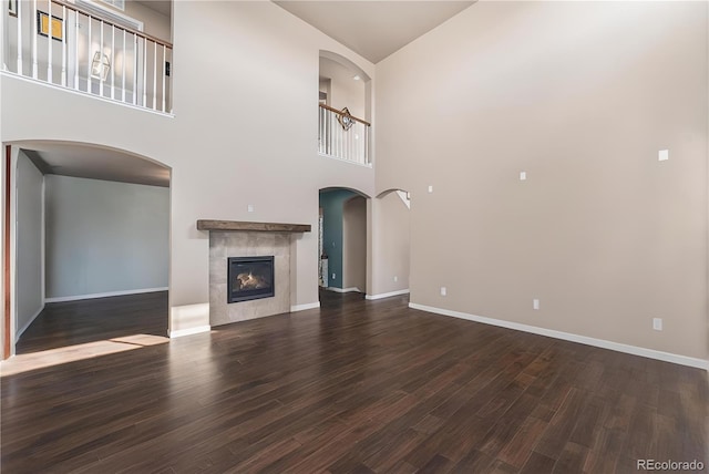 unfurnished living room with a tiled fireplace, wood finished floors, baseboards, and arched walkways