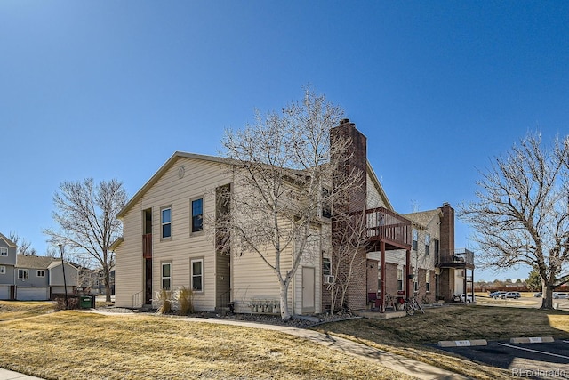 view of property exterior with a chimney, a patio area, a lawn, and a balcony