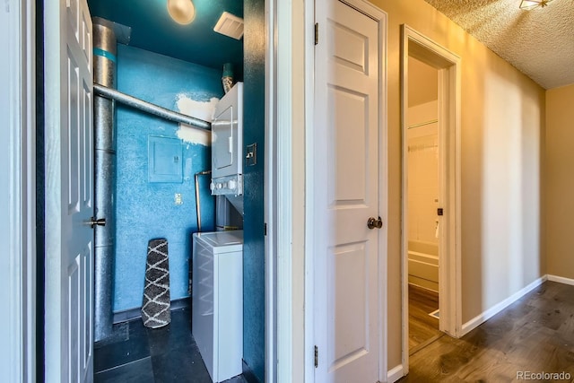 hall featuring stacked washer and clothes dryer, wood finished floors, baseboards, and a textured ceiling