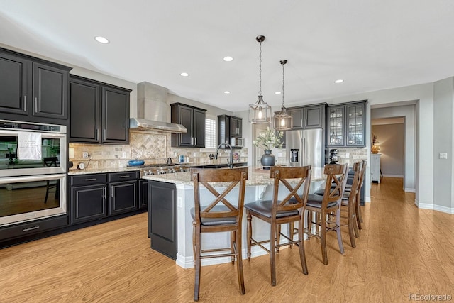 26566 E Peakview Dr, Aurora, CO 80016 - kitchen with backsplash, light wood-style floors, dark cabinetry, stainless steel appliances, and wall chimney exhaust hood