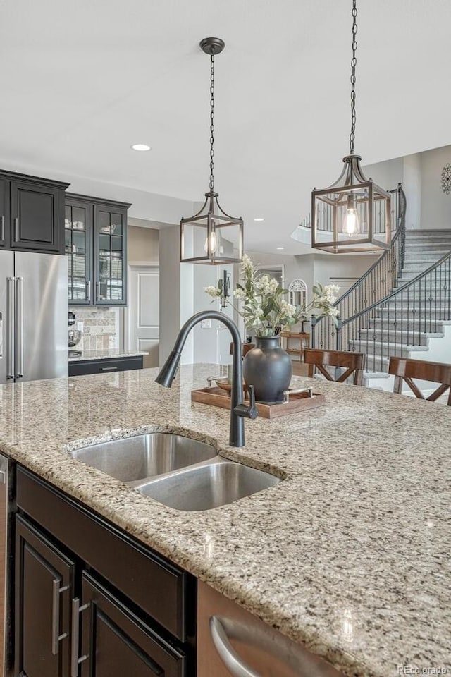 26566 E Peakview Dr, Aurora, CO 80016 - kitchen featuring pendant lighting, glass insert cabinets, light stone counters, a sink, and backsplash