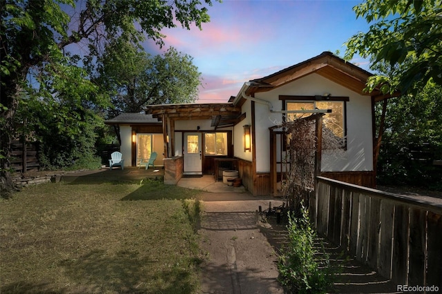 rear view of house featuring a patio area, fence, a lawn, and stucco siding