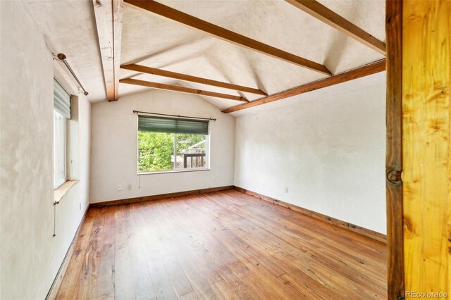 spare room featuring vaulted ceiling with beams, wood-type flooring, and baseboards