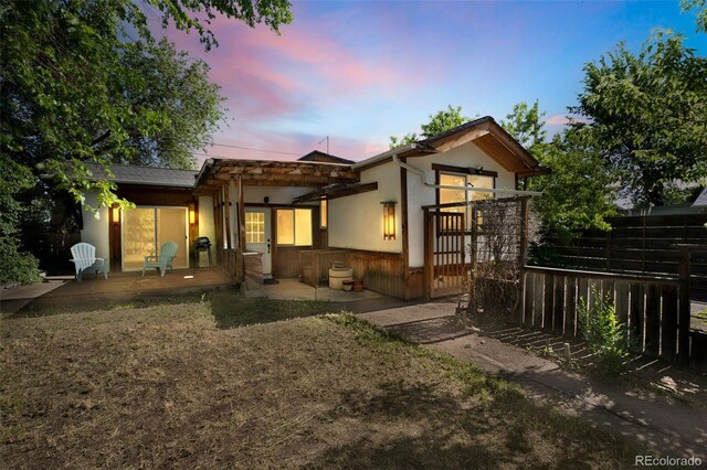 rear view of house featuring an attached garage, stucco siding, fence, and a patio