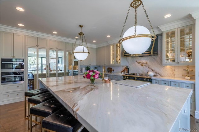 kitchen with a large island with sink, decorative backsplash, light stone counters, and ornamental molding