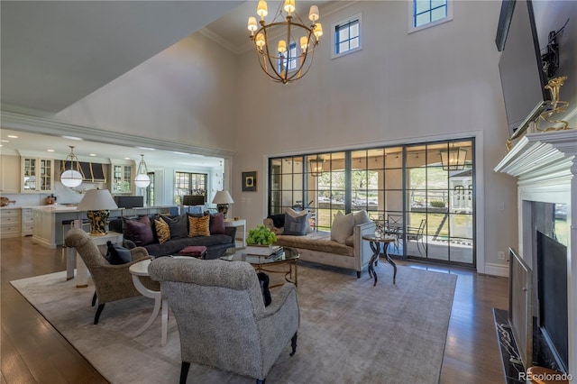 living area featuring a towering ceiling, wood finished floors, an inviting chandelier, ornamental molding, and a premium fireplace