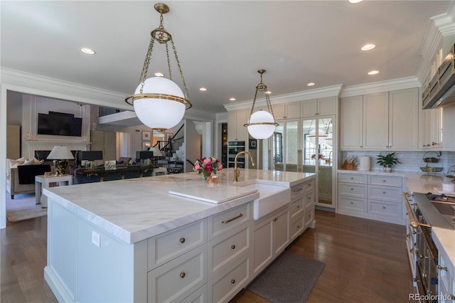 kitchen with decorative backsplash, light stone countertops, a large island with sink, a sink, and decorative light fixtures