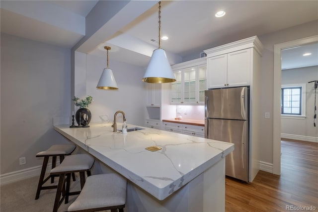 kitchen with a kitchen breakfast bar, a sink, freestanding refrigerator, glass insert cabinets, and white cabinetry