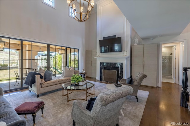 living area featuring an inviting chandelier, a towering ceiling, wood finished floors, a fireplace, and baseboards