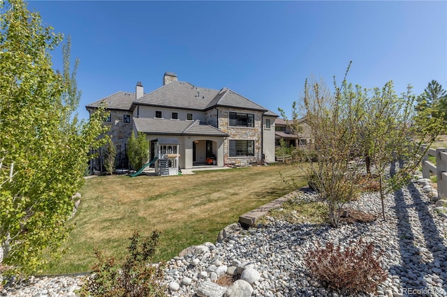back of property featuring fence, stone siding, a chimney, a patio area, and a lawn