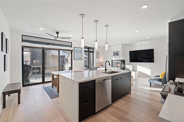 kitchen featuring dishwasher, sink, an island with sink, decorative light fixtures, and light hardwood / wood-style floors