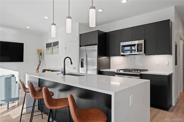 kitchen featuring decorative light fixtures, stainless steel appliances, a kitchen island with sink, and sink