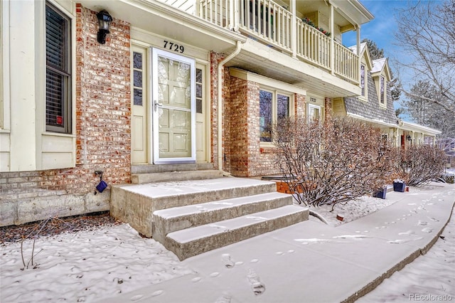 snow covered property entrance with a balcony and brick siding