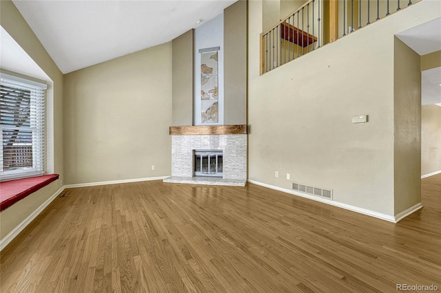 unfurnished living room with baseboards, visible vents, a glass covered fireplace, wood finished floors, and high vaulted ceiling