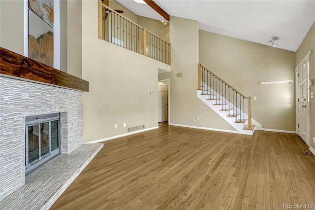 unfurnished living room featuring visible vents, wood finished floors, a tile fireplace, baseboards, and stairs