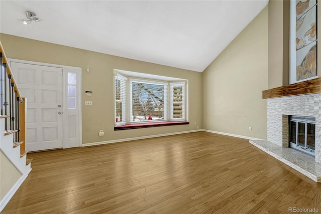 unfurnished living room featuring light wood-type flooring, lofted ceiling, a fireplace, and stairway