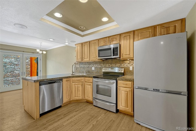 kitchen featuring stainless steel appliances, a tray ceiling, a peninsula, and dark countertops