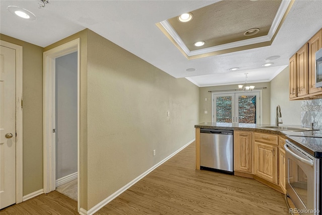 kitchen with a tray ceiling, crown molding, stainless steel appliances, light wood-style flooring, and a sink