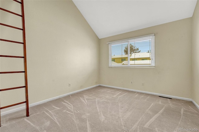 spare room with vaulted ceiling, baseboards, visible vents, and light colored carpet