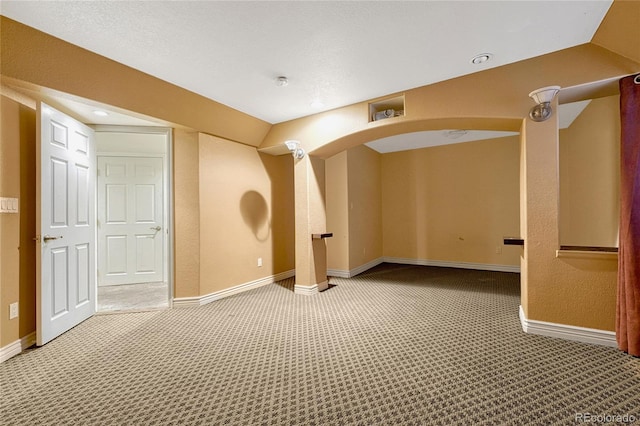 spare room featuring carpet floors, arched walkways, vaulted ceiling, and baseboards