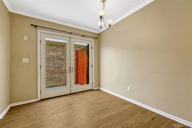 spare room featuring french doors, a notable chandelier, light wood finished floors, ornamental molding, and baseboards