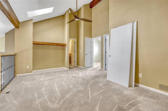 spare room with light colored carpet, a skylight, visible vents, baseboards, and beam ceiling