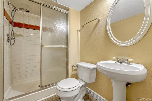 full bath with toilet, a stall shower, baseboards, and a textured wall