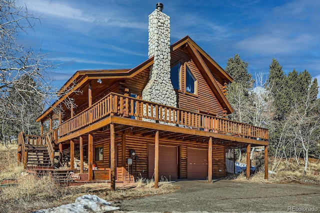 exterior space with log siding, a deck, a chimney, and aphalt driveway