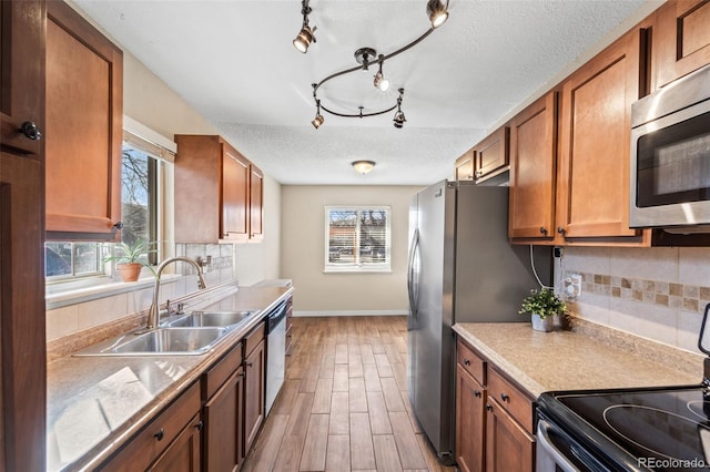 1940 Carmel Dr, Colorado Springs, CO 80910 - kitchen with brown cabinetry, a textured ceiling, a sink, stainless steel appliances, and baseboards