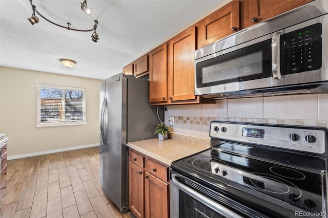 1940 Carmel Dr, Colorado Springs, CO 80910 - kitchen featuring baseboards, a textured ceiling, brown cabinetry, decorative backsplash, and appliances with stainless steel finishes
