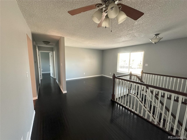 unfurnished room with a textured ceiling, baseboards, and wood finished floors